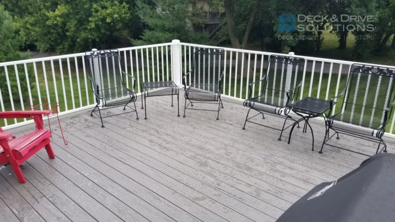 wrought iron chairs on gray composite deck with white railing and trees in back