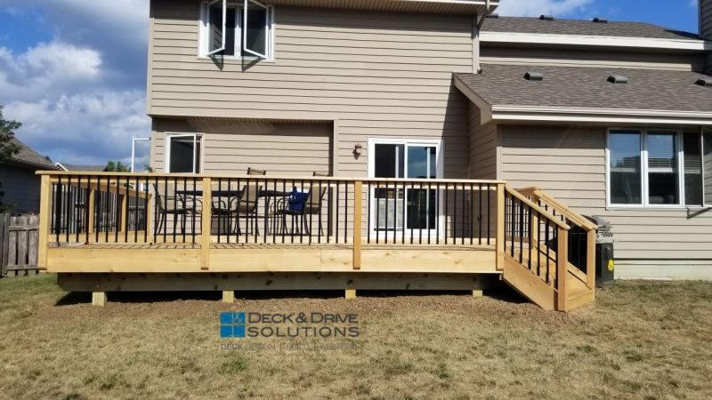 Cedar Deck close to ground with Cedar post rail and black aluminum deckorator spindles against a beige house