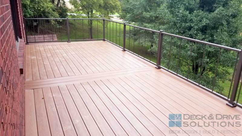 composite deck with picture frame board, bronze Westbury VertiCable Railing and many trees in backyard