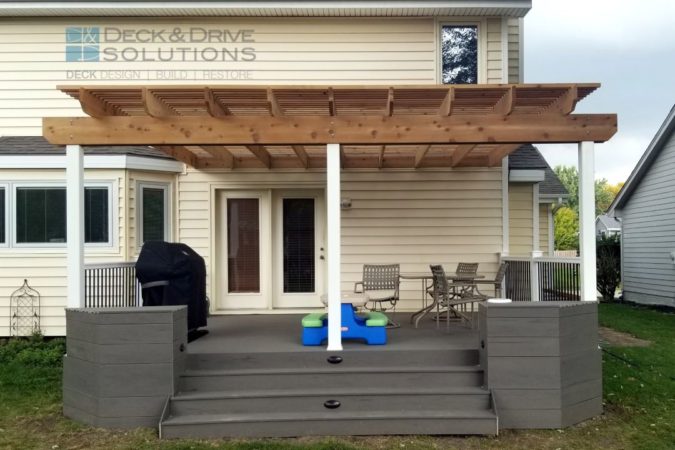 Cedar pergola with White PVC Post on top of a composite deck with wide stairs, built in planter box and deck lighting