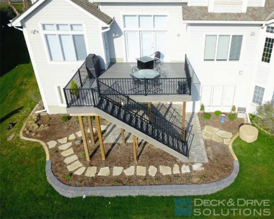 New walkout Composite Deck Timbertech Ashwood with Black Railing behind white house and landscaping below