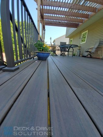 Close picture of composite deck flooring with bronze railing and pergola behind