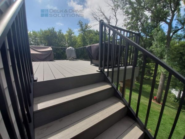 Deck stairs using timbertech silver maple, black metal westbury railing, on a sunny day