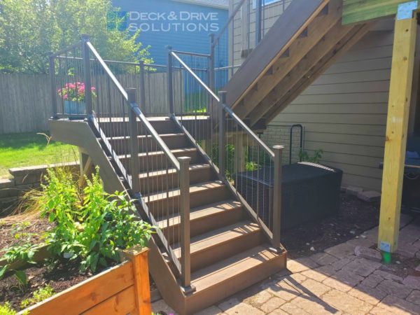 deck stairs landing on existing paver patio with flowers around