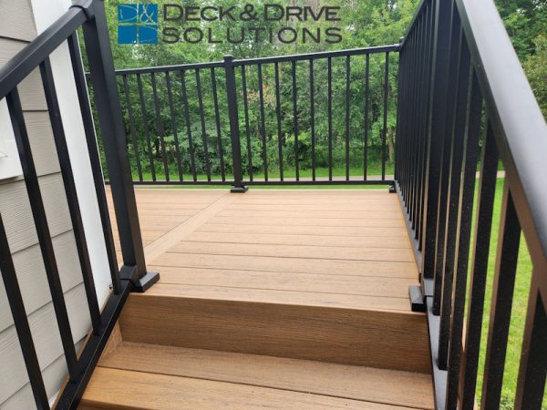 top of the stairs of a composite deck, black metal railing with woods in the background
